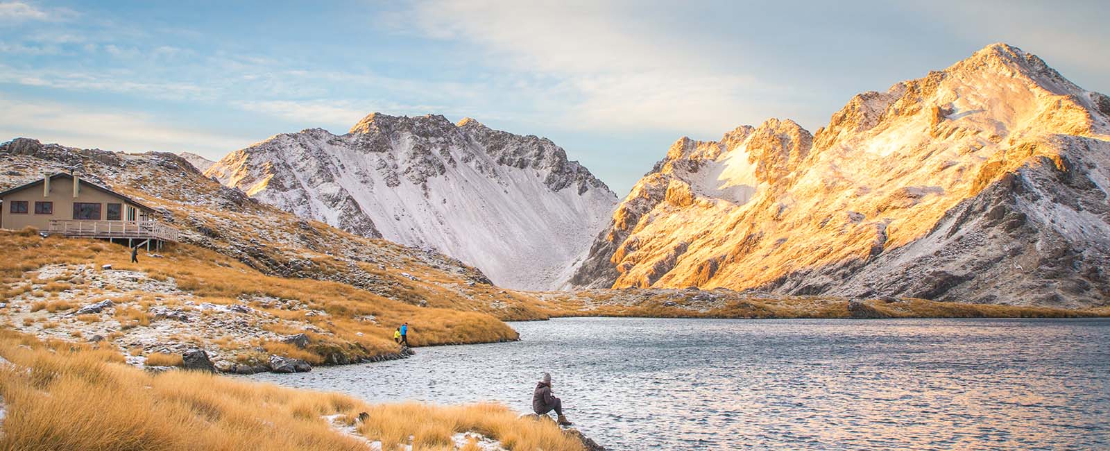 Person sitting beside a lake with two small mountain peaks behind them 